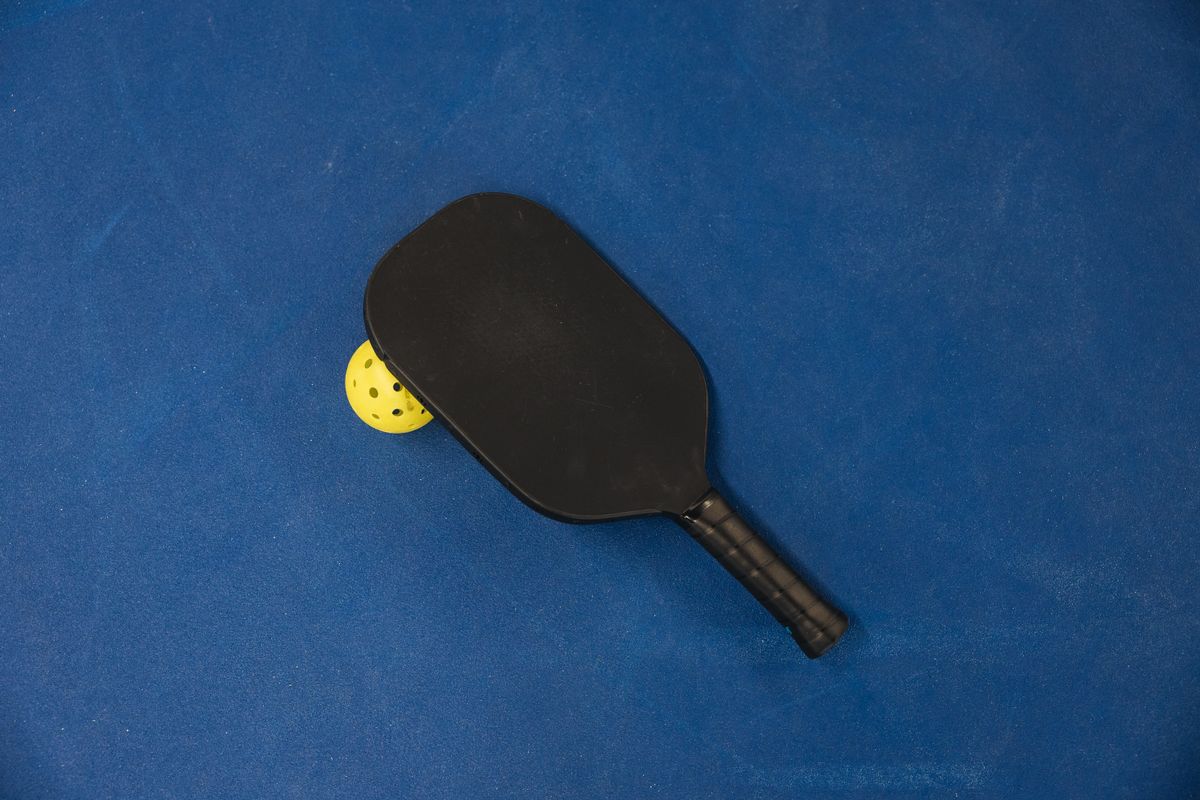 Close-up van een pickleball paddle en bal op blauwe ondergrond